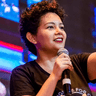 Lívia Gabos speaking into a handheld microphone on stage.